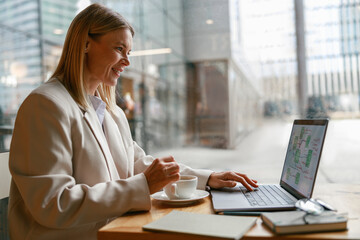 Wall Mural - Woman freelancer working on laptop and drinking coffee while sitting in cafe near window