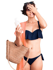 Wall Mural - Beautiful young woman with short hair wearing bikini holding sunscreen lotion stressed and frustrated with hand on head, surprised and angry face