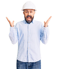 Wall Mural - Young handsome man wearing architect hardhat celebrating crazy and amazed for success with arms raised and open eyes screaming excited. winner concept