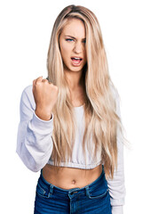 Canvas Print - Beautiful young blonde woman wearing casual white sweater angry and mad raising fist frustrated and furious while shouting with anger. rage and aggressive concept.