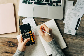 Top view of a work desk on which a woman keeps a budget using a calculator.