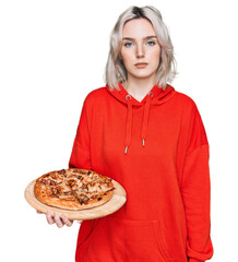 Wall Mural - Young blonde girl holding italian pizza thinking attitude and sober expression looking self confident