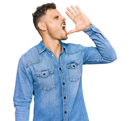 Poster - Young hispanic man wearing casual denim jacket shouting and screaming loud to side with hand on mouth. communication concept.