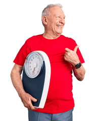 Sticker - Senior handsome grey-haired man holding weighing machine pointing thumb up to the side smiling happy with open mouth