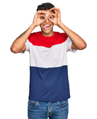 Canvas Print - Young handsome african american man wearing casual clothes doing ok gesture like binoculars sticking tongue out, eyes looking through fingers. crazy expression.