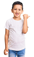 Wall Mural - Little cute boy kid wearing casual white tshirt smiling with happy face looking and pointing to the side with thumb up.