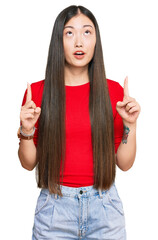 Canvas Print - Young chinese woman wearing casual clothes amazed and surprised looking up and pointing with fingers and raised arms.