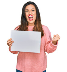 Sticker - Beautiful hispanic woman holding blank empty banner screaming proud, celebrating victory and success very excited with raised arms