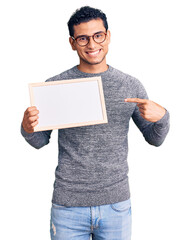 Wall Mural - Hispanic handsome young man holding blank empty banner smiling happy pointing with hand and finger