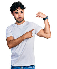 Poster - Hispanic young man with beard wearing casual white t shirt strong person showing arm muscle, confident and proud of power