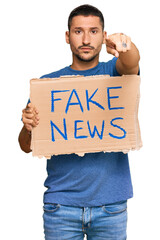 Wall Mural - Handsome man with tattoos holding fake news banner pointing with finger to the camera and to you, confident gesture looking serious