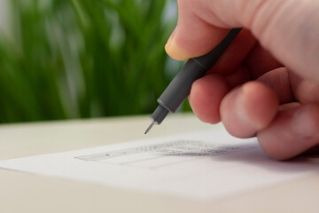 A male hand draws with a pen liner on a piece of paper. Artistic tool. Idea, hobby and creativity. Closeup photo