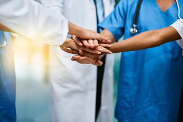 Poster - In it to saves lives together. Shot of a group of unrecognisable medical practitioners joining their hands together in unity.