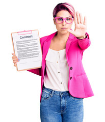 Canvas Print - Young beautiful woman with pink hair holding clipboard with contract document doing stop sing with palm of the hand. warning expression with negative and serious gesture on the face.