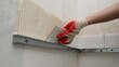 Industrial close-up of a worker's hand applying cement adhesive for laying ceramic tiles. Attaching tiles to the wall. Laying tiles on the wall.