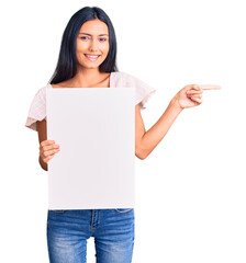 Canvas Print - Young beautiful latin girl holding blank empty banner smiling happy pointing with hand and finger to the side