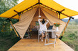 © Ananass - young woman working on a laptop while sitting near a big tent in nature