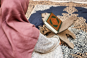 Wall Mural - woman sitting in the mosque and reading a Quran - open for prayers.background of the Muslims around the world placed on a wooden board Quran in the mosque 