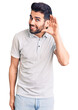 © Krakenimages.com - Young handsome man with beard wearing casual polo smiling with hand over ear listening an hearing to rumor or gossip. deafness concept.