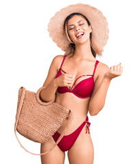 Sticker - Young beautiful woman wearing bikini and hat holding summer wicker handbag screaming proud, celebrating victory and success very excited with raised arms