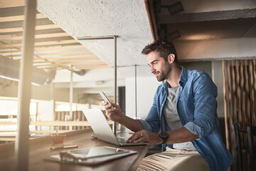 Aufkleber - The hard work that goes into running a cafe. Shot of a handsome young man using a laptop and phone in a coffee shop.