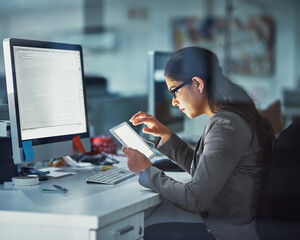 Poster - online and on the job. shot of a young businesswoman working late in the office.
