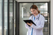 © Songsak C - Portrait of confident positive female doctor holding clipboard when standing at her office desk