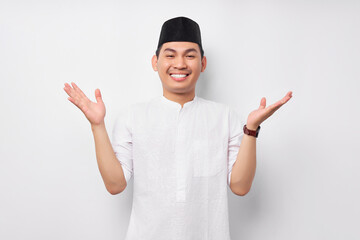 Wall Mural - Smiling friendly handsome young Asian Muslim man wearing Arabic costume standing with wide raised arms and welcoming Ramadan isolated over white background. People religious Islamic lifestyle concept