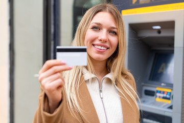 Wall Mural - Young pretty blonde woman holding a credit card at outdoors with happy expression