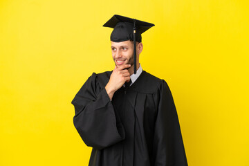 Wall Mural - Young university graduate caucasian man isolated on yellow background looking to the side