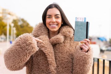 Poster - Young woman holding a passport at outdoors with surprise facial expression