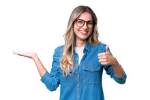 Young Uruguayan Woman Over Isolated Background Holding Copyspace Imaginary On The Palm To Insert An Ad And With Thumbs Up