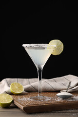 Wall Mural - Martini glass of refreshing cocktail with lime and sugar on wooden table against black background