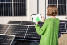 Young Woman Monitors Energy Production From The Solar Power Plant With A Digital Tablet. View On Tablet Screen With Running Program. Concept Of New Technologies In Alternative Energy
