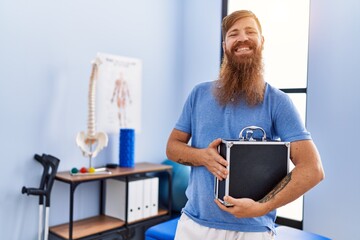 Sticker - Young redhead man wearing physiotherapist uniform holding briefcase at physiotherapy clinic