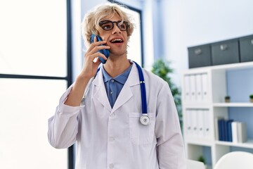 Wall Mural - Young blond man doctor smiling confident talking on smartphone at clinic