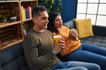 Canvas Print - Man and woman couple drinking coffee sitting on sofa at home