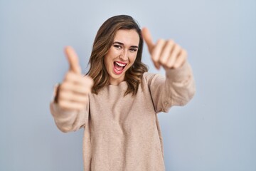 Poster - Young woman standing over isolated background approving doing positive gesture with hand, thumbs up smiling and happy for success. winner gesture.