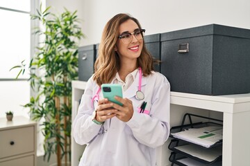 Canvas Print - Young woman wearing doctor uniform using smartphone at clinic