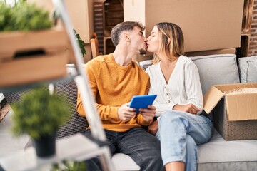 Sticker - Young man and woman couple using touchpad sitting on sofa at new home