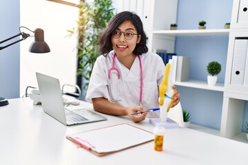 Canvas Print - Young latin woman wearing doctor uniform holding anatomical model of knee at clinic