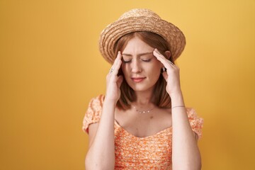 Wall Mural - Young redhead woman standing over yellow background wearing summer hat with hand on head for pain in head because stress. suffering migraine.