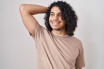 Poster - Hispanic man with curly hair standing over white background smiling confident touching hair with hand up gesture, posing attractive and fashionable