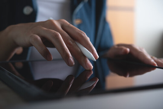 Woman working and using digital tablet pc, finger touching on touchpad screen on office table, close up