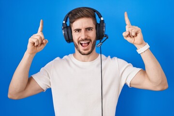 Poster - Hispanic man with beard listening to music wearing headphones smiling amazed and surprised and pointing up with fingers and raised arms.