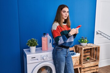 Poster - Young woman using smartphone waiting for washing machine at laundry room