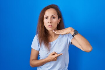 Poster - Brunette woman standing over blue background cutting throat with hand as knife, threaten aggression with furious violence