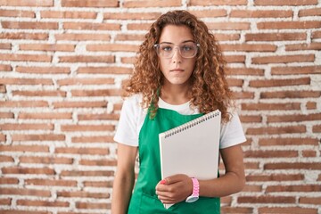 Poster - Young caucasian woman holding art notebook relaxed with serious expression on face. simple and natural looking at the camera.