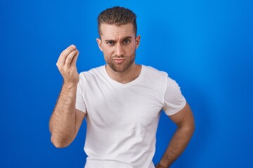 Poster - Young caucasian man standing over blue background doing italian gesture with hand and fingers confident expression