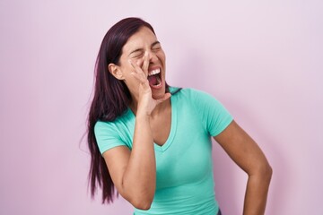 Poster - Young hispanic woman standing over pink background shouting and screaming loud to side with hand on mouth. communication concept.